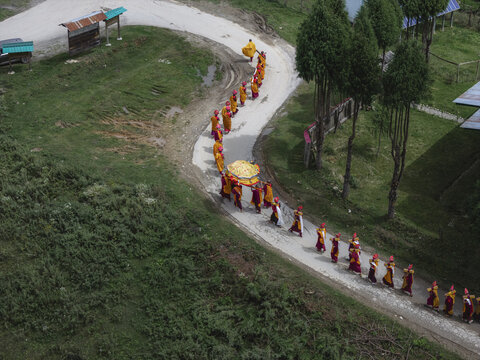 Aerial view of a solemn procession of monks in vibrant robes winds along a pale path near Gangtey Monastery, a tranquil scene of faith, Gangtey Monastery, Wangdue Phodrang, Bhutan.