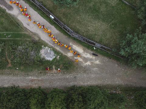Aerial view of monks with orange robes walking along the dusty pathways near lush greenery and a stone wall, Gangtey Monastery, Wangdue Phodrang, Bhutan.