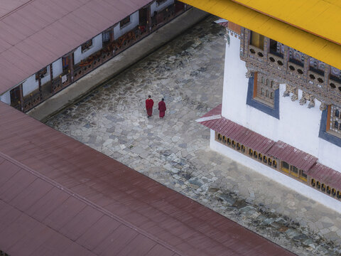 Aerial view of two monks in vibrant red robes walking across the stone courtyard of Gangtey Monastery, Nubding, Wangdue Phodrang, Bhutan.