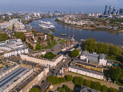 Aerial view of the Cutty Sark and the Royal Naval College nestle by the Thames, where a cruise ship glides past the modern skyline, Greenwich, London, United Kingdom.