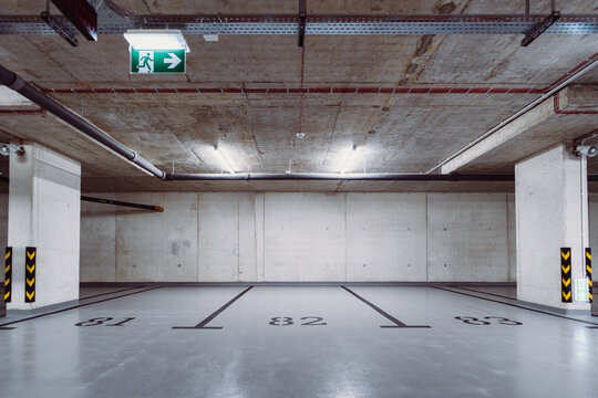 Empty underground parking spaces with concrete walls and emergency exit sign