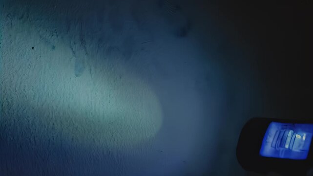 Blue light beam from a handheld flashlight illuminates a textured wall, revealing patterns and shadows as the light source moves across the surface in a dynamic sequence