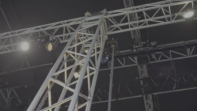 Metal truss structure with lighting fixtures and chains is shown from below, highlighting the intricate design and functionality in a performance setup with visible equipment