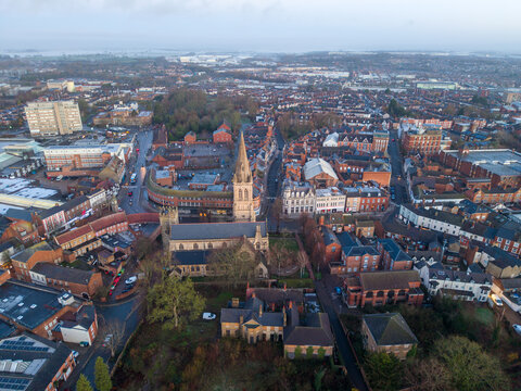 Aerial view of the Holy Trinity Church's spire pierces the skyline amidst the urban tapestry, contrasting with the muted tones of the surrounding buildings, Rugby, England, United Kingdom.