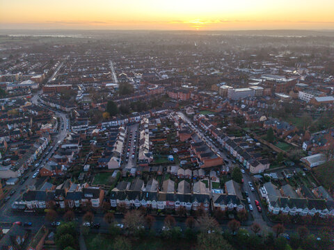 Aerial view of rooftops glow with the soft light of the setting sun, casting long shadows over quiet streets and orderly rows of houses, Rugby, England, United Kingdom.