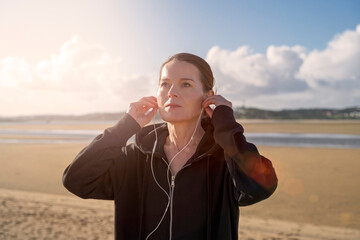 Woman on beach wearing hoodie adjusting earphones