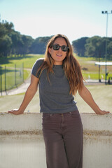 A woman wearing sunglasses and a gray shirt stands on a railing