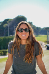 A woman with long hair and sunglasses is smiling for the camera