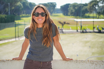 A woman wearing sunglasses and a grey sweater stands on a ledge