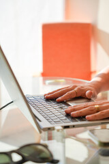 A person is typing on a laptop computer in front of an orange chair