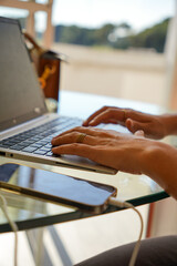 A woman is typing on a laptop while holding a cell phone