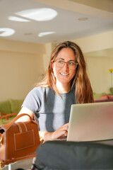 A woman is sitting at a table with a laptop and a brown purse