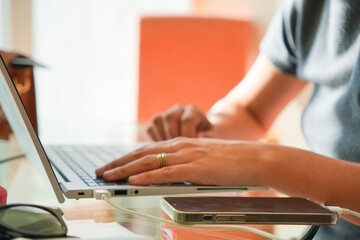 A person is typing on a laptop while holding a cell phone