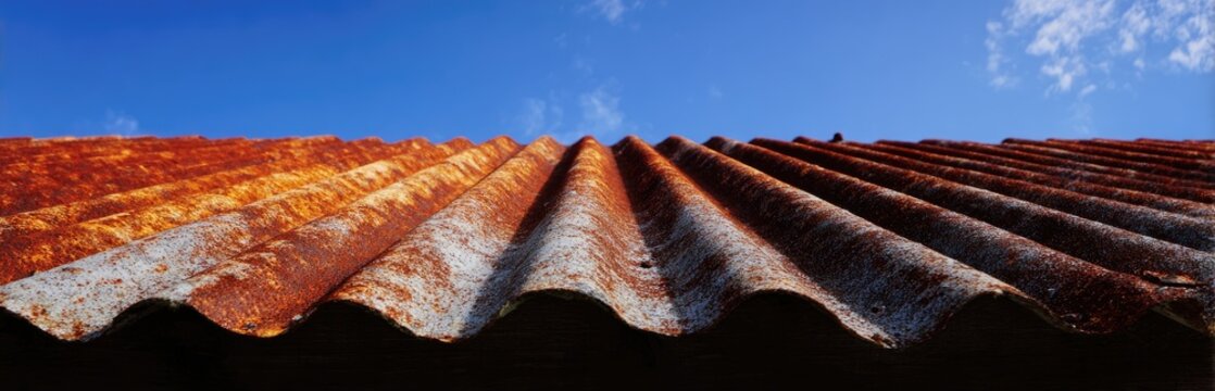 Close-up of weathered corrugated metal roofing with vibrant rust tones against a bright blue sky