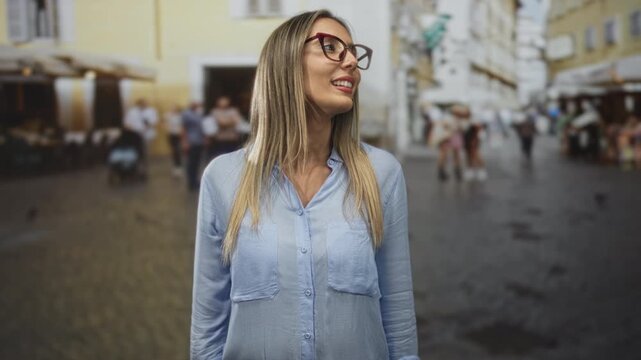 Woman smiling wearing glasses and blue shirt while standing on street plaza with blurred crowd; confidence travel.