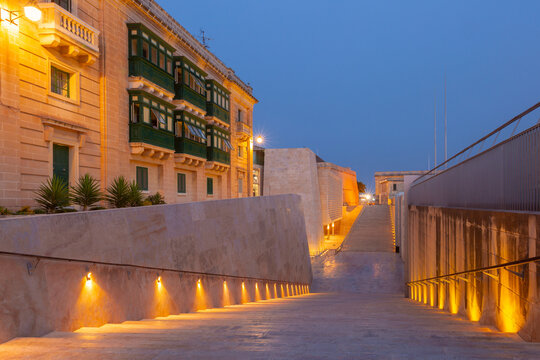 Illuminated stone steps leading to Valletta s City Gate in Malta at dusk.