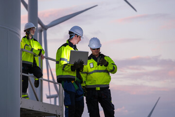 Workers check equipment and review data at a wind turbine site during sunset in a renewable energy project
