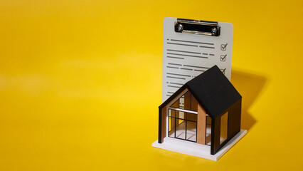 Small house model and completed inspection checklist document on yellow background.