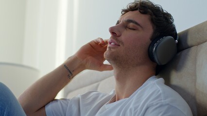 Relaxed Caucasian man in bedroom at home wearing headphones enjoying music sound calm male guy...