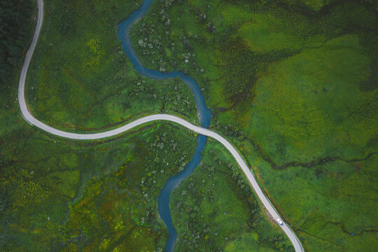 Aerial view of a winding road bisecting a vibrant green landscape, with a blue river snaking through the valley, Phobjikha Valley, Wangdue Phodrang, Bhutan.