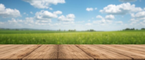 Naklejka premium Blurry green landscape and blue sky with clouds, wooden table surface visible