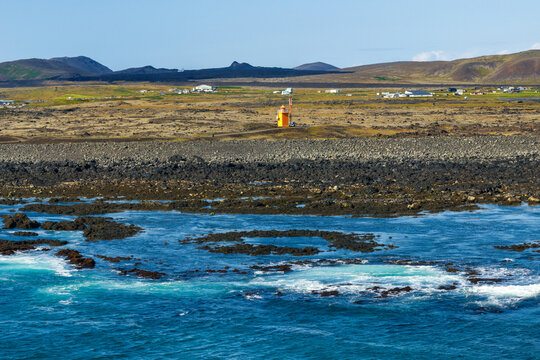 drone view of the Hopsnes Peninsula and reefs near Grindavik in southwestern Iceland with the orange lighthouse