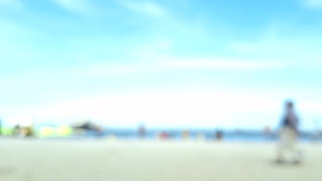 The blurred background shows many people relaxing and playing on a sandy beach, with a bright blue sky in the morning.