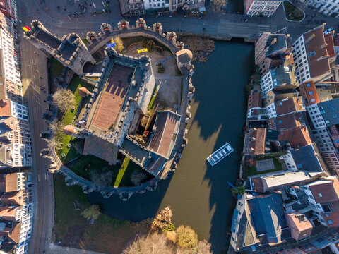 Aerial view of the Gravensteen castle's formidable stone walls meet the tranquil waters of the canal, a stark contrast amidst the urban landscape, Ghent, Flanders, Belgium.
