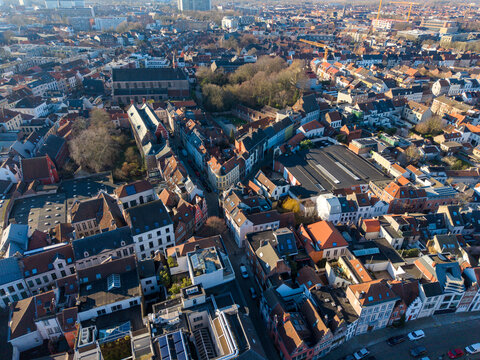 Aerial view of the vibrant tapestry of terracotta rooftops and winding streets, punctuated by the solemn grandeur of a church and a small forest, Ghent, Flanders, Belgium.