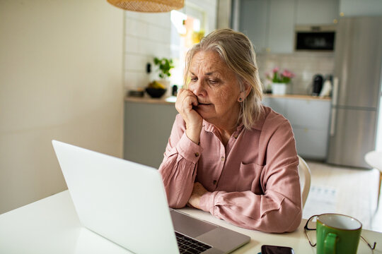 Senior woman worried at laptop in home kitchen