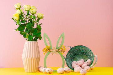 Decorative spring arrangement with flowers and Easter eggs on a yellow table against a pink background
