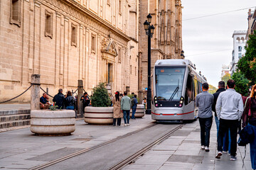 Obraz premium Tram is moving in front Cathedral Seville with tourists walking, life on streets Andalusian city. Urban transport in Spain.