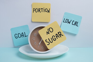 Alarm clock on plate with no sugar and low calorie notes. Intermittent fasting and healthy eating schedule.
