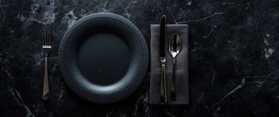 Top view of black craft plate, cutlery, and napkin on dark table - table setting with copy space