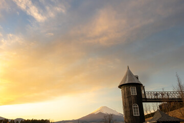 Fototapeta premium 夕日に染まる空と雪化粧した富士山とアンティークな塔の風景, 