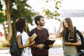 Three international students standing in a park and holding a books
