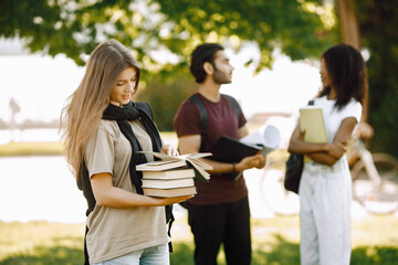 Three international students standing in a park and holding a books