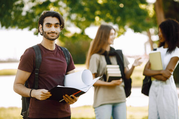 Three international students standing in a park and holding a books