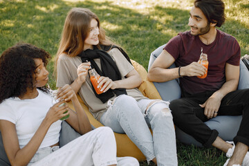Three friends with bottles of juice sitting on the bean bag chairs in a park