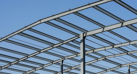A complex grid of heavy gray steel beams forms the framework of a large industrial building under construction against a clear sky background ,steel ,construction ,future