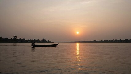 Naklejka premium Silhouette of small fishing boat on river at beautiful calm sunset with glowing sun on horizon
