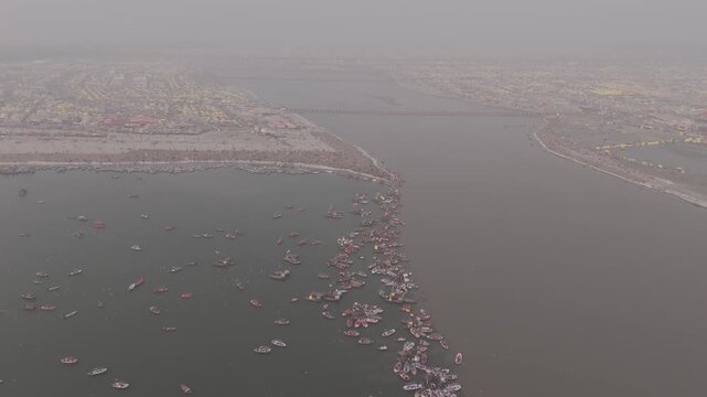 Aerial drone view of the Sangam during Magh Mela in Prayagraj. Boats move across the meeting point of the Ganga, Yamuna, and mythical Saraswati, with pilgrims gathering along the riverbanks. The scene