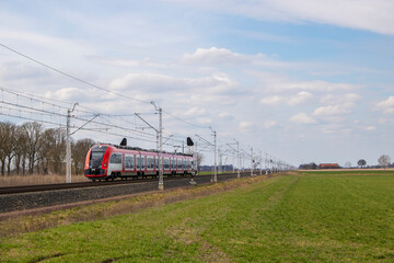 Czerwony pociąg z pasażerami pędzi po torach © Erap2