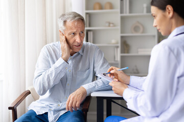 Obraz premium Senior male patient reporting ear pain to female doctor during medical visit in modern clinic office, focused on hearing health and symptom assessment