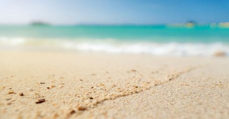 close-up of sandy beach and blurry sea with waves rolling onto the shore under a blue summer sky where footprints lead toward the horizon of the vast ocean nature © noppadon