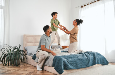 Family in a cozy home interior, sitting on a large comfortable bed in pajamas, holding their son by...