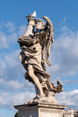 Obraz premium Seagull perched atop an angel statue in Rome, Italy, against a clear blue sky—classic marble sculpture blending wildlife, history, and timeless European art.
