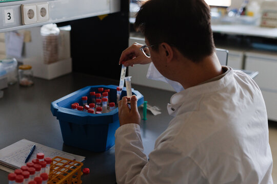 A man, a chemist seen from the back of the shoulder is working in a lab, pipetting some liquids. 