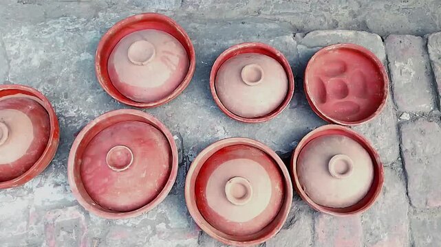 Traditional handmade clay pottery and cake molds placed on the ground for drying under the sun.