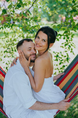 A couple embraces lovingly in a vibrant hammock under leafy trees, exuding warmth and intimacy on a sunny day.